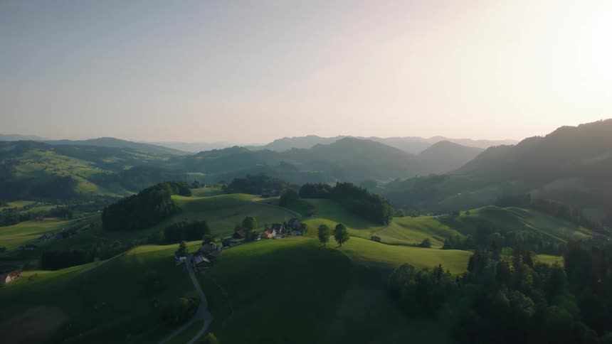 A beautiful aerial view of a picturesque Swiss countryside with rolling green hills and farms at sunset