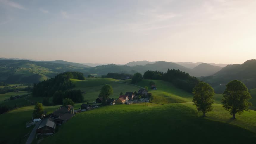 An idyllic aerial view captures a small village nestled within the rolling green hills of the Swiss countryside at sunrise