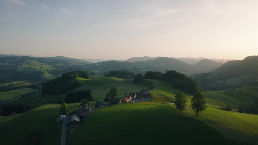 A tranquil aerial view shows the sun rising over the lush, rolling green hills of a picturesque European countryside