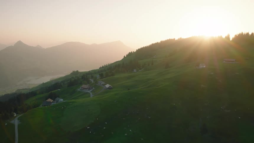 A beautiful aerial view reveals the rolling green hills of the Swiss Alps as the sun rises over the mountains