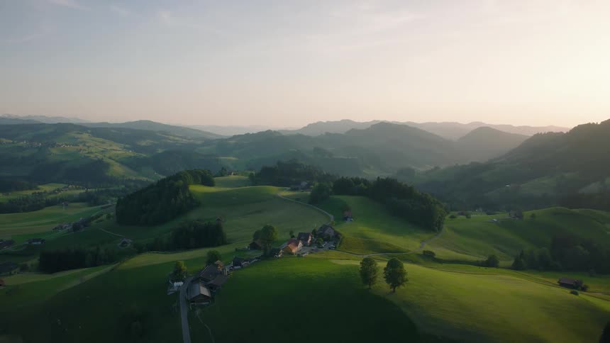 A stunning aerial view pulls back to reveal a tranquil rural landscape of lush green rolling hills and mountains at sunrise
