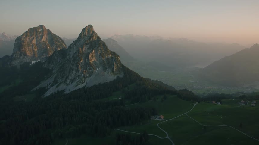 A stunning wide shot of majestic mountain peaks illuminated by the soft light of sunrise, overlooking a lush green valley