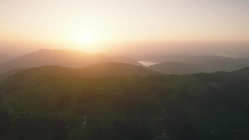 A serene aerial view shows the golden sun rising over a vast, green mountain landscape