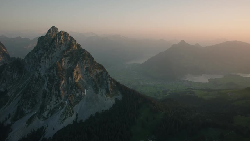An epic aerial view pulls back from a majestic mountain peak overlooking a beautiful hazy valley at sunrise