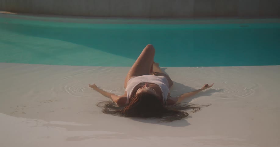 A woman in a white swimsuit lies back and relaxes in the shallow water of a resort swimming pool