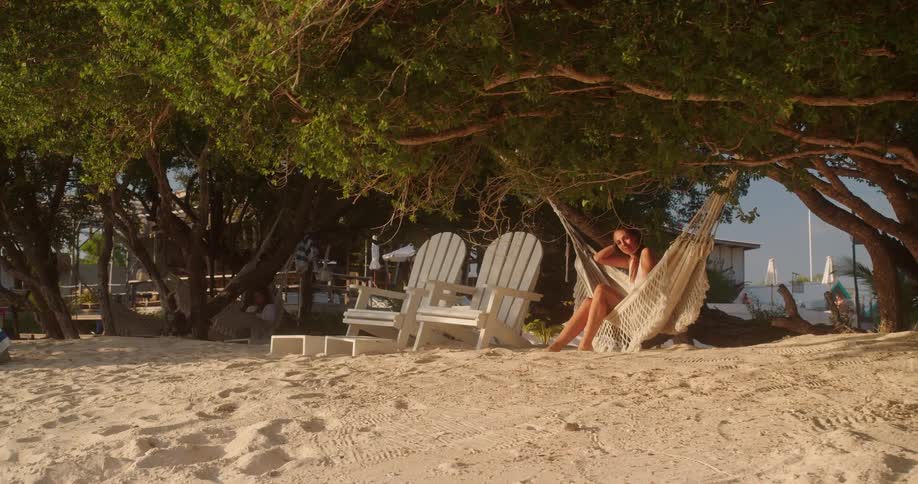 A serene woman in a swimsuit enjoys a peaceful afternoon in a hammock on a tropical beach under the shade of lush green trees