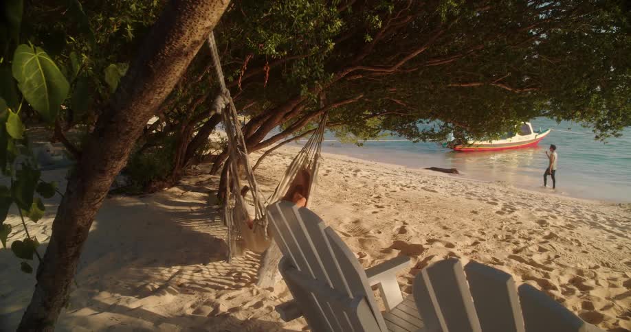 A serene shot of a woman relaxing in a hammock on a sandy beach, pulling back to reveal the tranquil oceanside