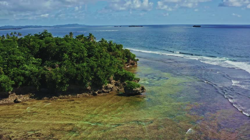 Expansive aerial view of a lush tropical island coastline with a shallow reef and the vast blue ocean on a sunny day