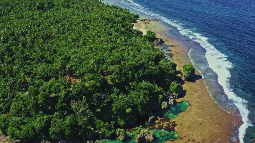 High angle aerial view of a stunning turquoise natural rock pool on a lush tropical coastline, with the vast blue ocean beyond
