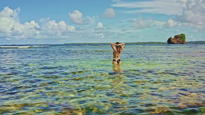 A woman in a bikini wades through the crystal-clear waters of a tropical lagoon, enjoying the serene beauty of her island getaway