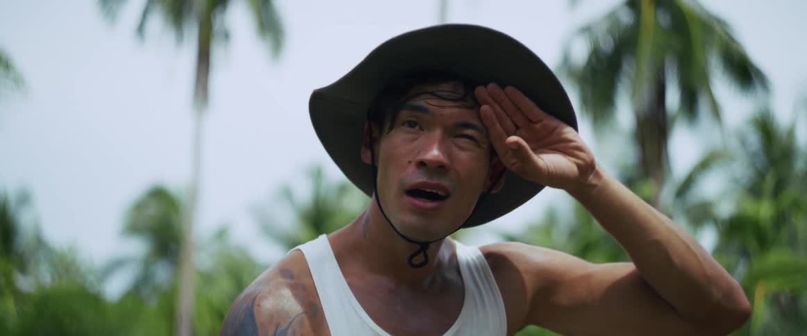 Close-up of an exhausted and sweaty man in a wide-brimmed hat taking a break in a lush jungle