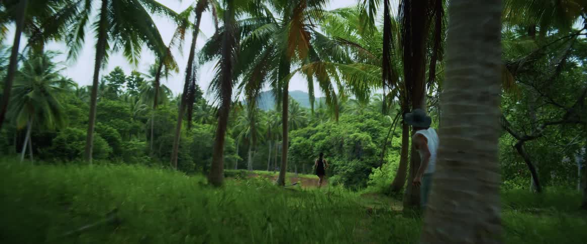 Slow motion footage shows a man running through a lush tropical jungle, following a woman ahead