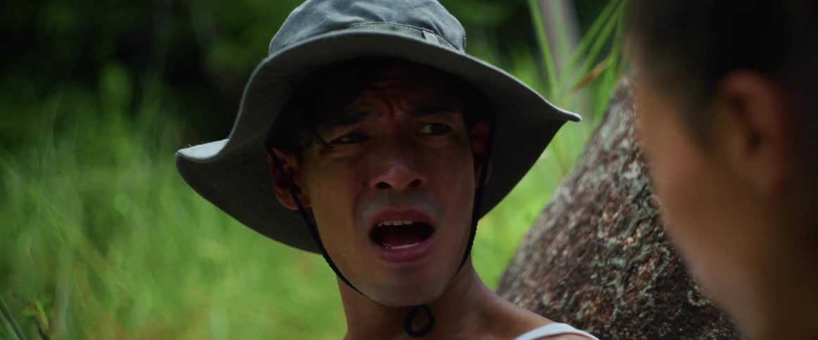 Close up of a sweaty and scared man in a hat having a tense conversation in a tropical forest