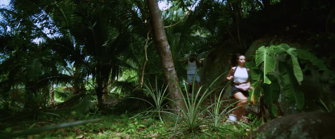 A panicked man and woman run through a lush, dense jungle in a suspenseful chase scene