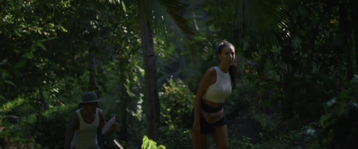 A young couple enjoys a slow-motion hike uphill through a lush and vibrant tropical jungle