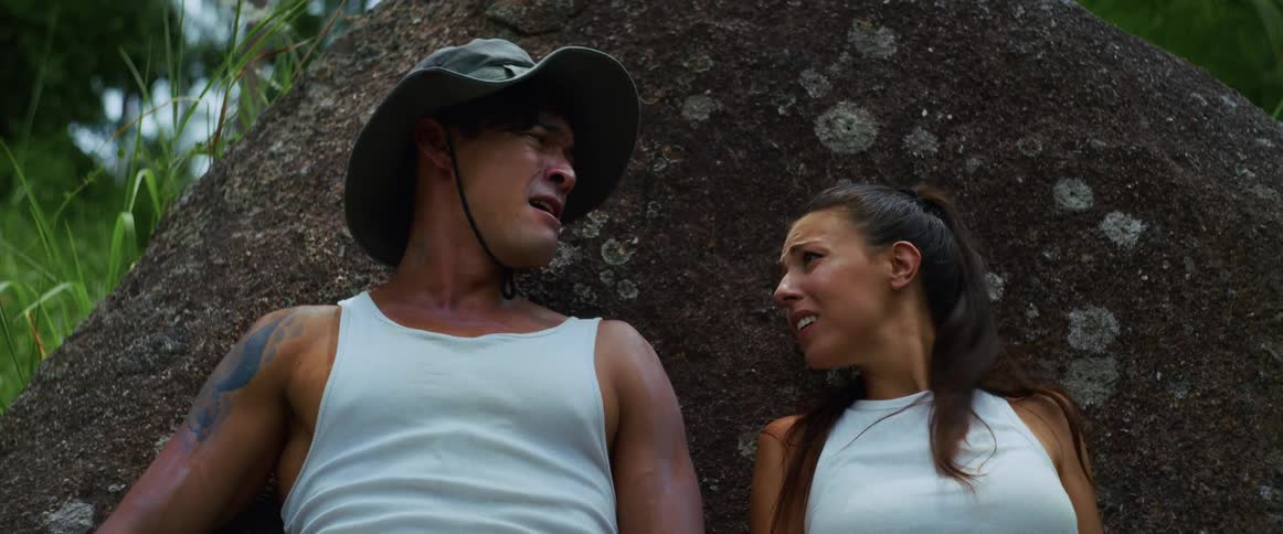 An exhausted and distressed couple rests against a large boulder in the jungle before the man suddenly jumps up and leaves