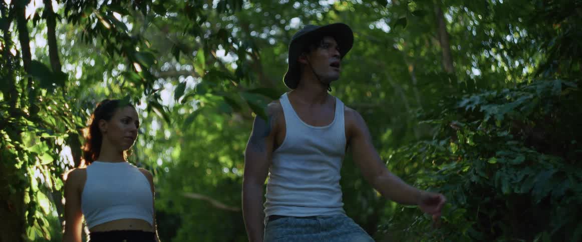 A couple on an expedition through a lush, sun-drenched jungle stops to cautiously observe their surroundings
