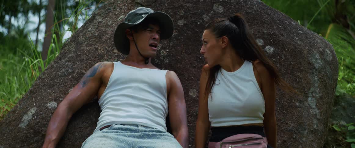 An exhausted couple rests against a rock while lost on a difficult hike through a dense jungle