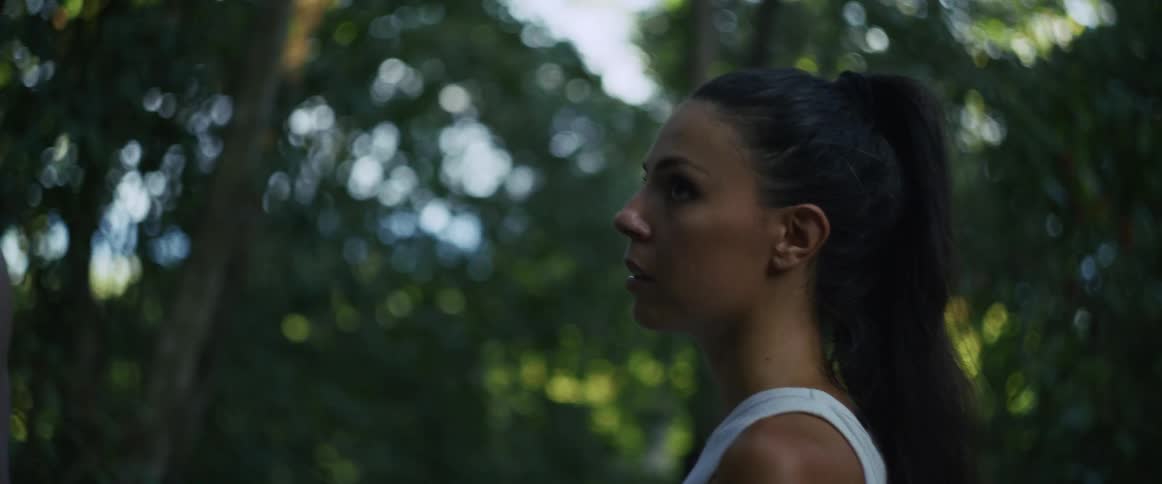 A terrified woman looks up in shock as she explores a dense, green jungle with her companion