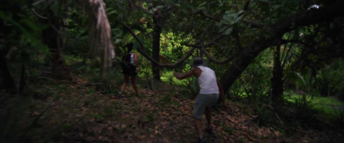 A man and woman run away through a lush tropical jungle in dramatic slow motion