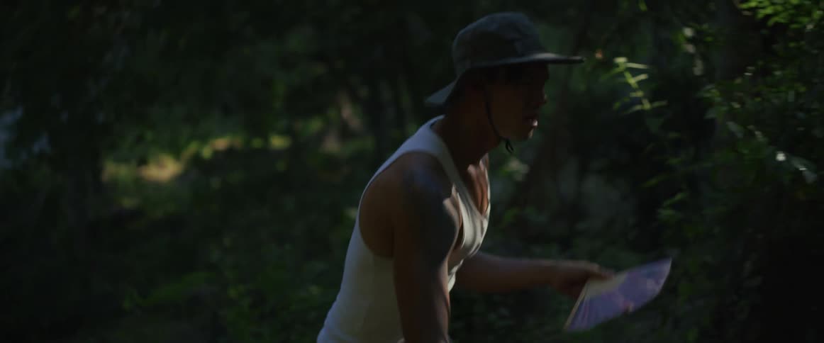 A sweaty and exhausted man in a hat desperately fans himself while struggling through a hot and humid jungle