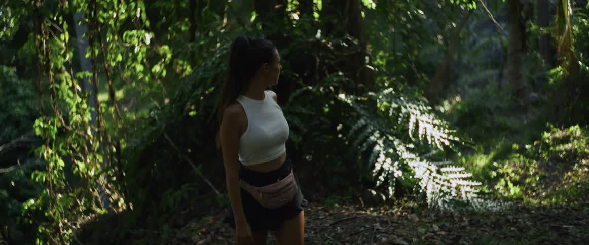 A couple walks in slow motion along a path through a lush, sunlit tropical jungle