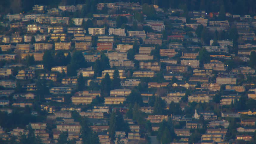 A fast whip zoom from a coastal city view into a close-up of houses nestled on a steep, forested hill at golden hour