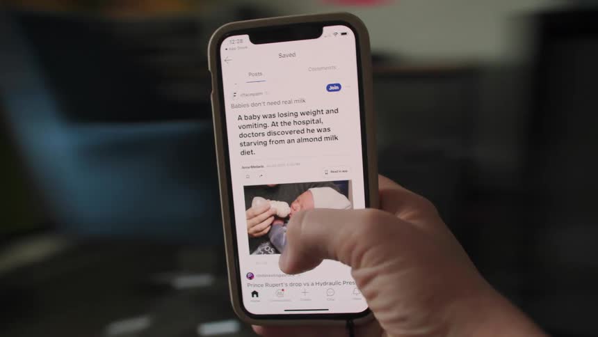 A person's hand holds a smartphone while endlessly scrolling through saved posts on a social media app