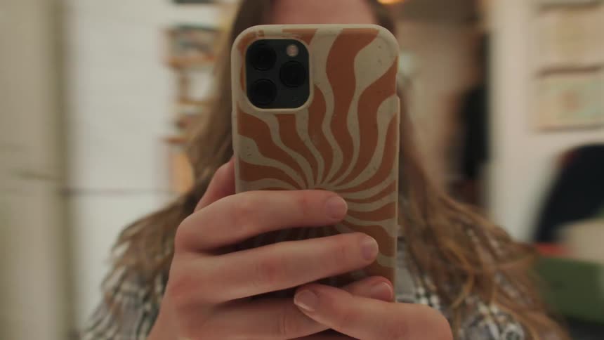 A woman holds a smartphone with a retro-style case covering her face as the room spins around her in a dizzying, seamless loop