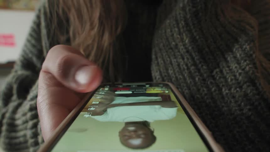 A close-up view from below of a person's hands scrolling endlessly through a social media feed on their smartphone
