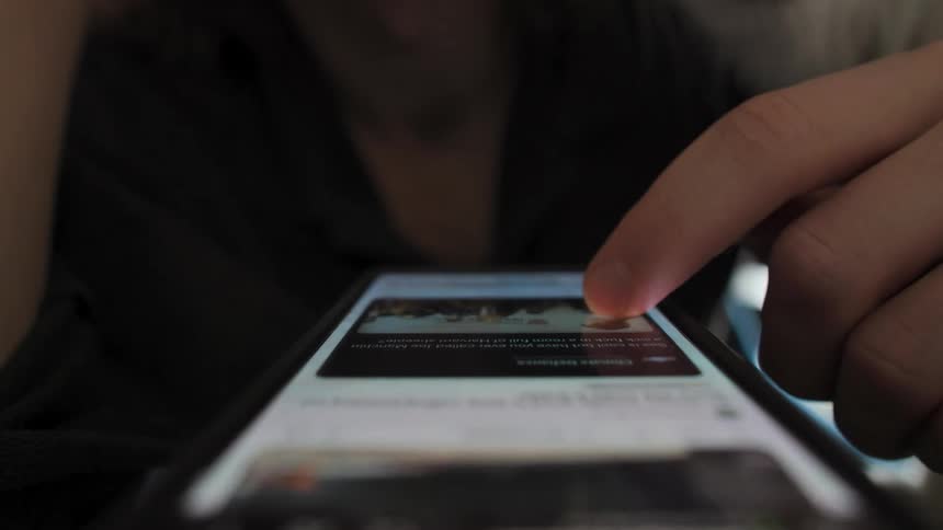 A close-up of a person endlessly scrolling through a social media feed on their smartphone as their cat curiously sniffs the screen