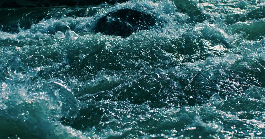 A hypnotic slow-motion shot of powerful turquoise river rapids flowing and creating white water