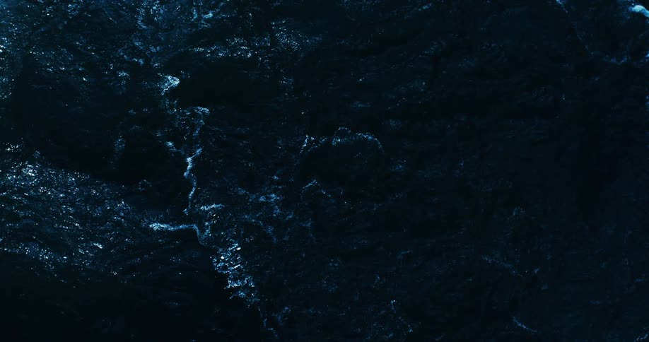 A mesmerizing top-down view of dark, deep blue ocean water slowly churning and creating a textured surface