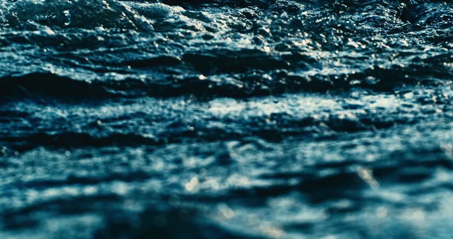 An intense close-up of dark blue water churning in a hypnotic slow-motion shot, highlighting the texture and movement of the surface