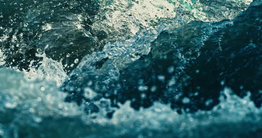 A super slow-motion close-up of churning blue-green water splashing in the bright sunlight