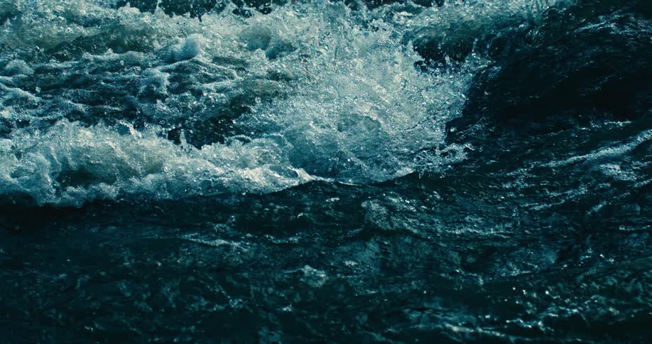 A mesmerizing slow-motion closeup of turbulent deep blue water churning and splashing