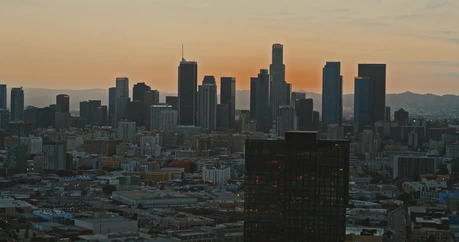 The impressive Los Angeles downtown skyline is silhouetted against a beautiful orange sunset sky in a slow aerial pullback
