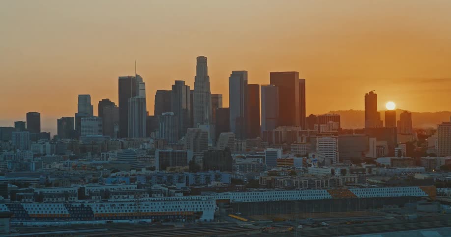 An aerial view captures the iconic downtown Los Angeles skyline bathed in the warm, golden light of a beautiful sunset