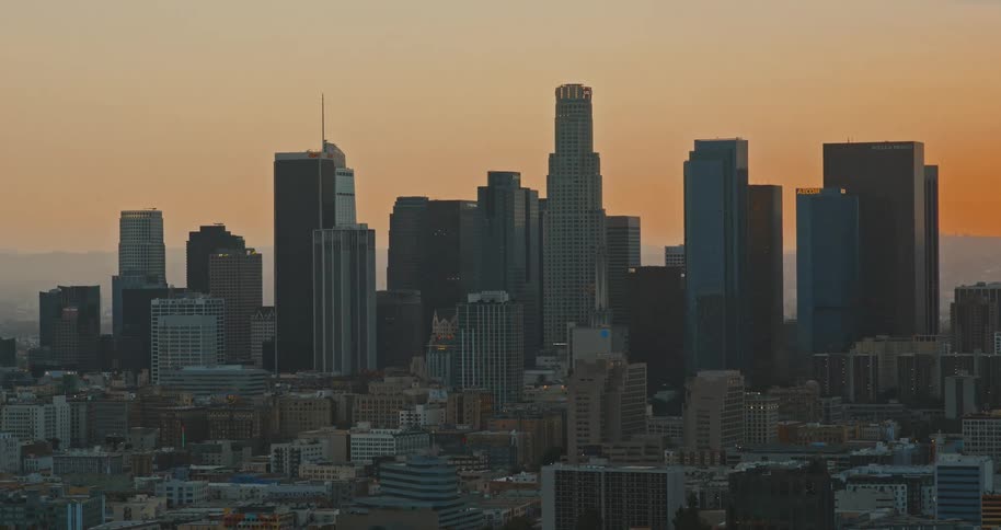 A slow zoom out reveals the downtown Los Angeles skyline as the sun sets, casting a warm orange glow across the city