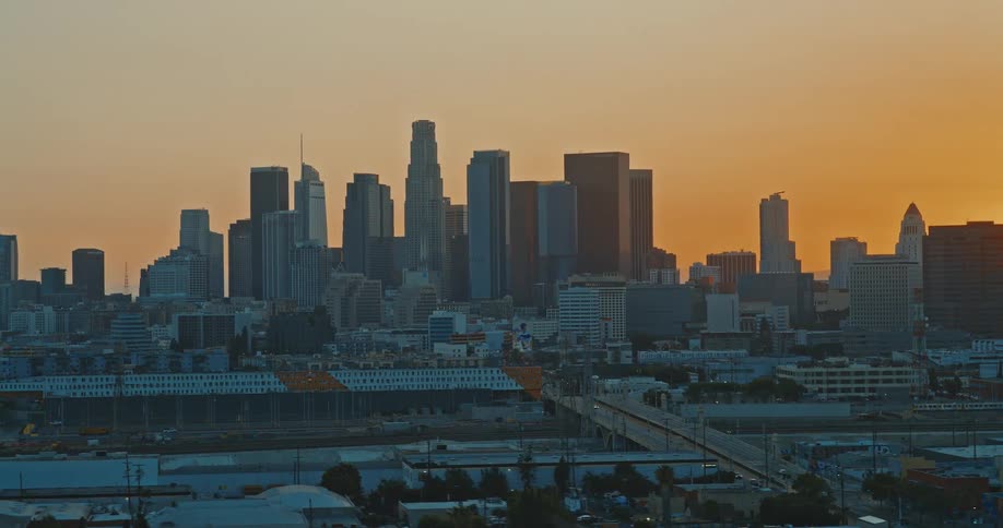 A slow-pushing aerial shot of the iconic downtown Los Angeles skyline during a warm, vibrant sunset