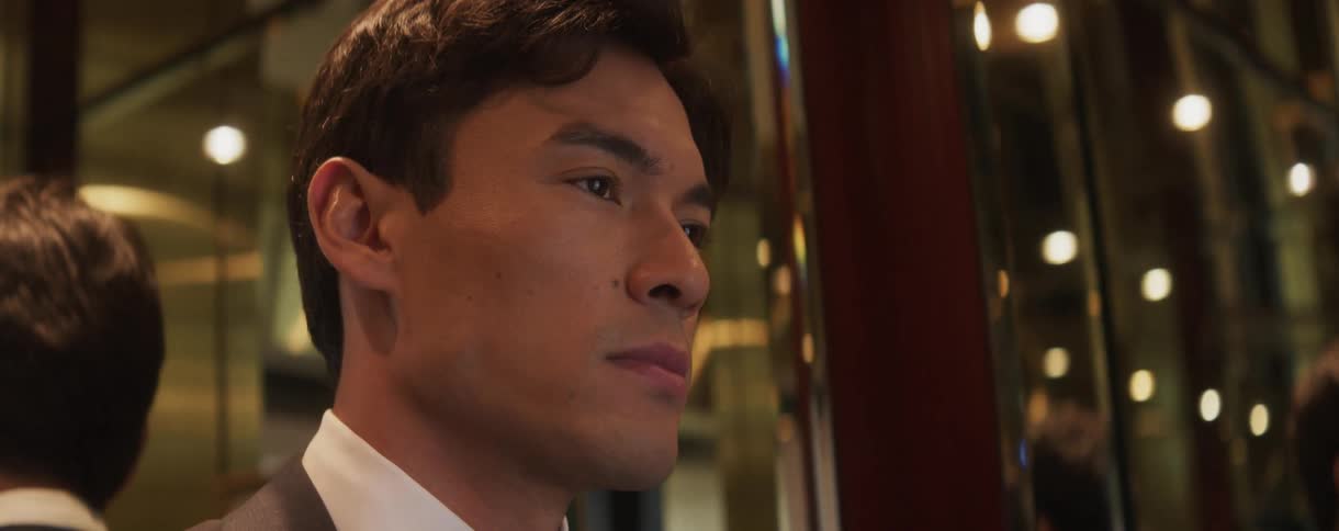 A handsome man in a tuxedo looks on with a serious and pensive expression in a luxurious setting at night
