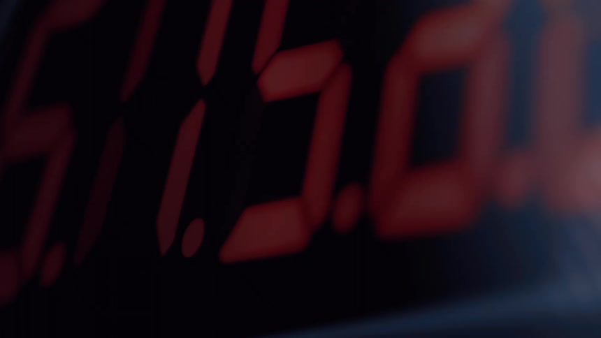 An extreme close-up, out-of-focus shot of a digital clock with red numbers rapidly counting down