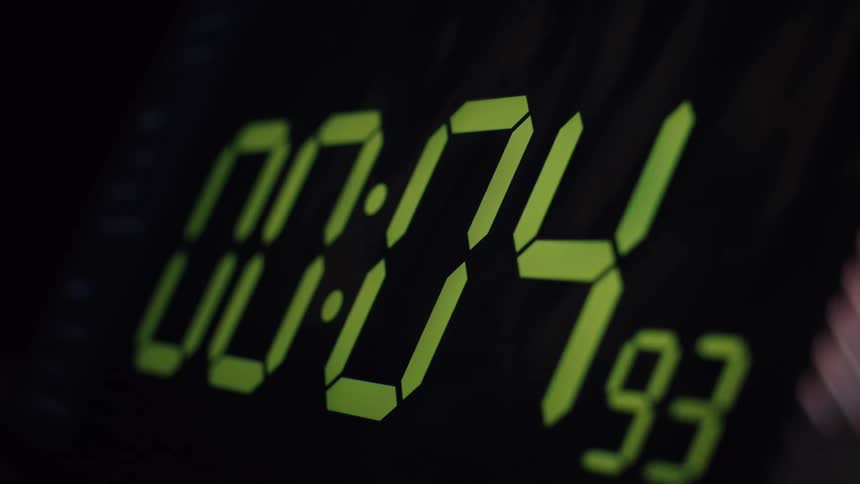 A close-up of a green digital timer display counting down from ten seconds to zero in the dark