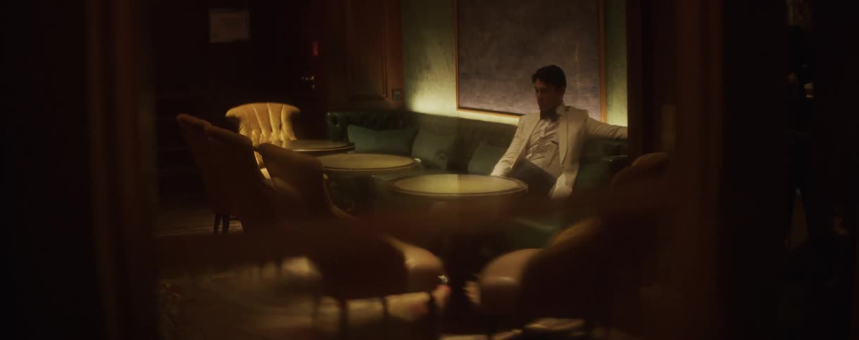 A dapper man sits pensively in a secluded booth of a sophisticated, empty bar