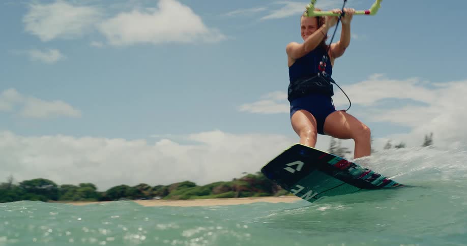 An athletic woman smiles while kitesurfing in the ocean, gliding past the camera in stunning slow motion
