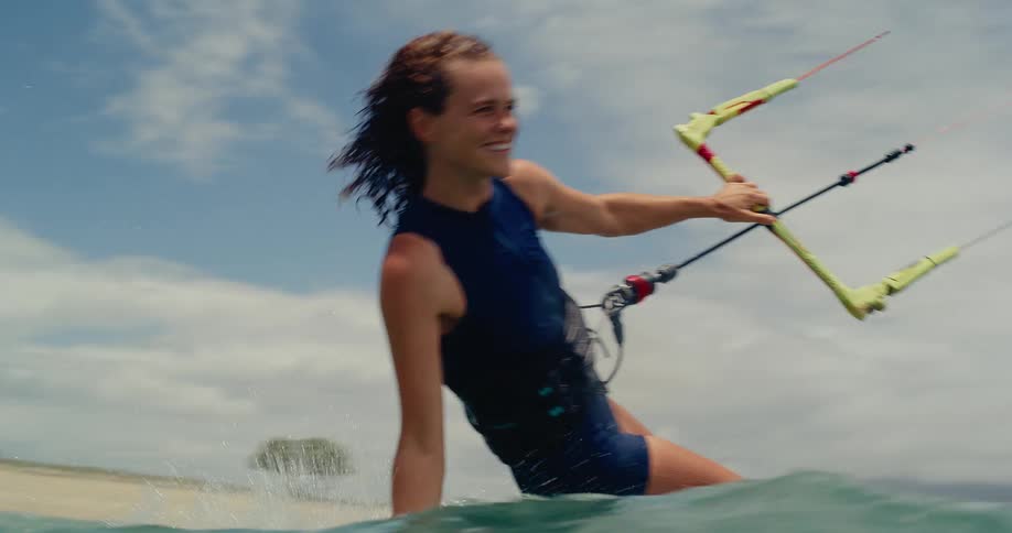 An athletic woman smiles as she kitesurfs past the camera in slow motion on a beautiful tropical day