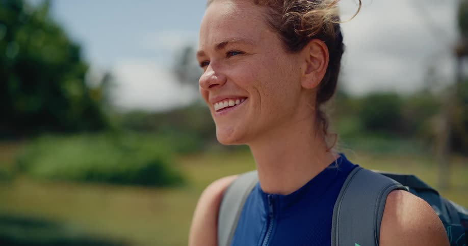 Slow motion close-up of a happy, athletic woman with a backpack, smiling as the wind blows through her hair