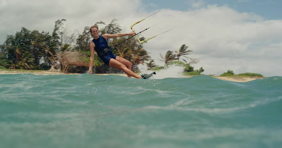A happy athletic woman kitesurfs along a tropical beach shoreline in beautiful slow motion