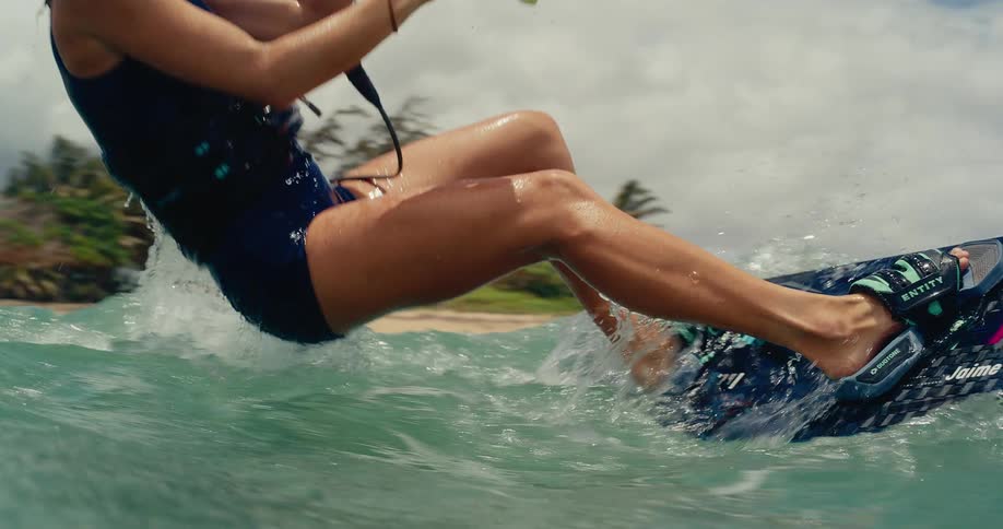 A woman kitesurfer prepares to ride in the ocean before taking off in slow motion on a tropical beach