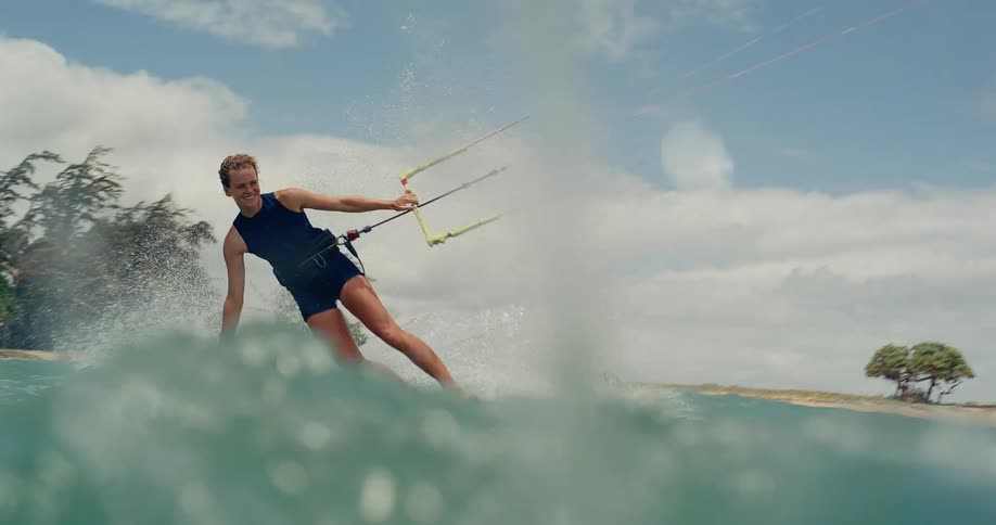 A happy woman kitesurfing in the ocean glides past the camera in an epic slow motion shot from the water